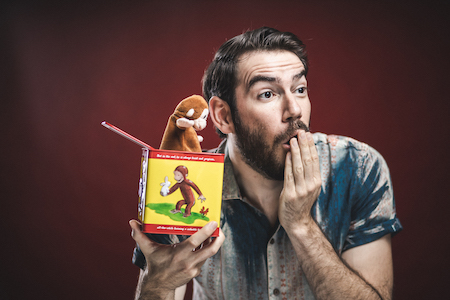 Esteban Gast holds a Curious George jack-in-the-box toy, looking whimsically surprised
