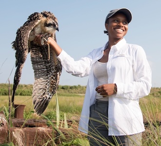 Diamon Clark smiles while holding a large raptor out in a field
