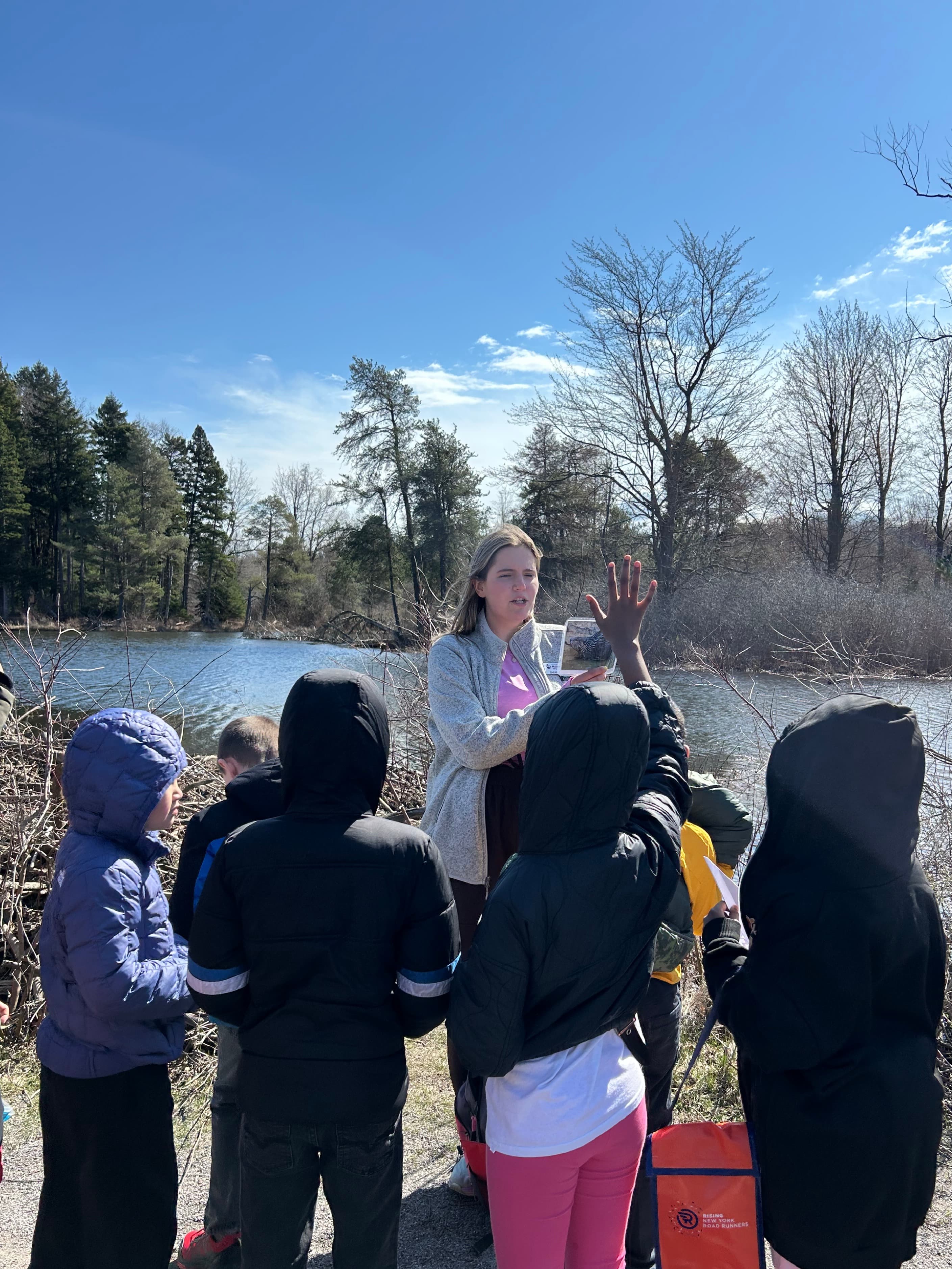 Students gather around a teacher at the edge of a river