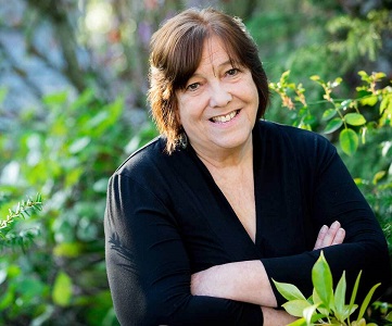 Portrait of a smiling, short-haired woman surrounded by green leaves