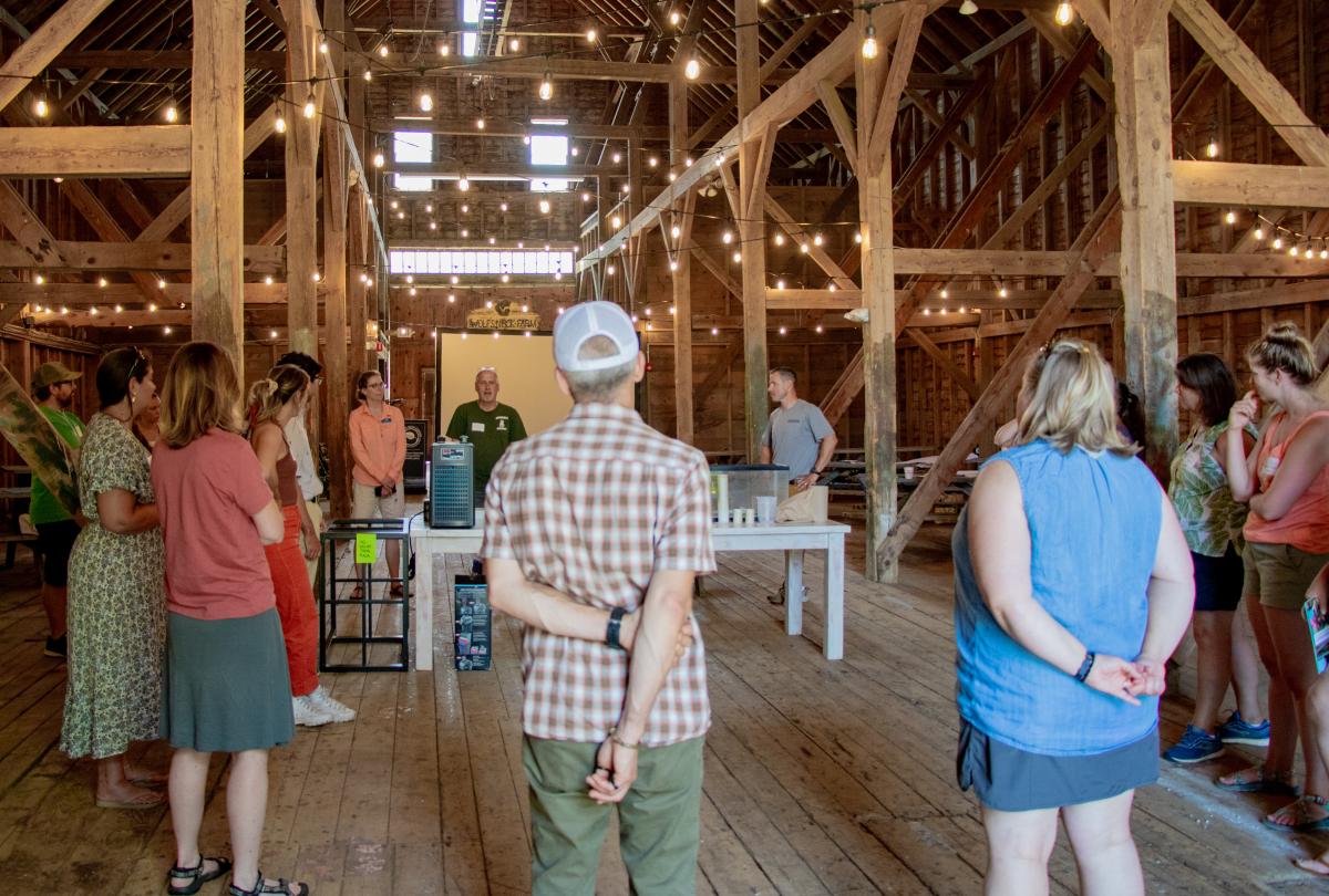 A group of teachers gathers around a table with an aquarium display in a large barn. Photo credit: Kathy Tenga-Gonzalez, Maine Sea Grant