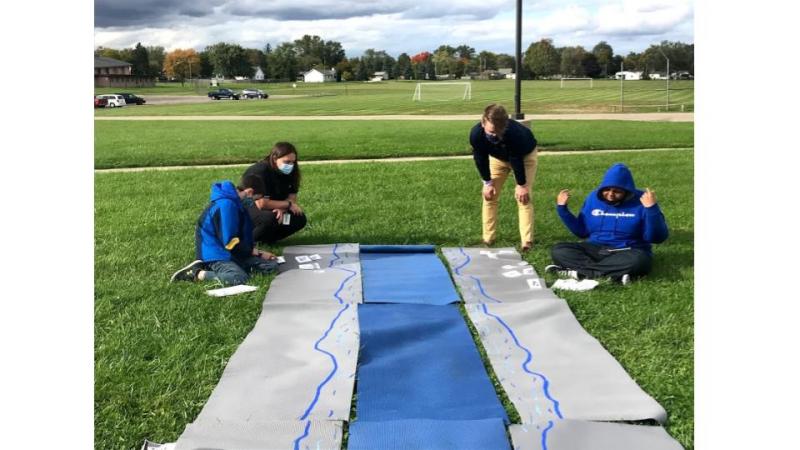 Two youth and two teachers view a river community made out of yoga mats and activity cards