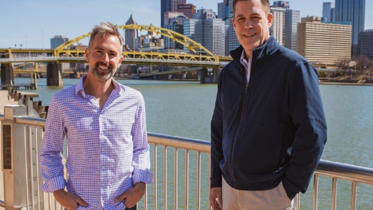 Ryan Rydzewski and Greg Behr stand in front of a yellow bridge in Pittsburgh, Pennsylvania.