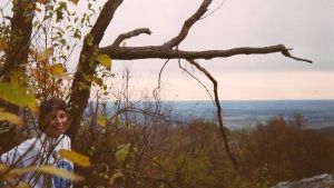 A younger Stacie standing amount trees on a rocky bluff.