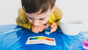 A young child hovers over a multi-colored pH result graph after completing a water pH test.