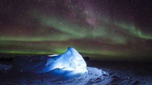 Illuminated ice shines bright in white and blue. Stars dance with green as the Northern Lights twinkle above. 