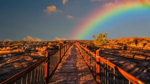 Photo of stone bridge in a rocky landscape with a rainbow arching from the center of the photo to the right