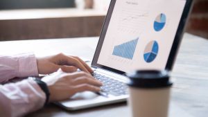 Close up of hands on a laptop keyboard. Laptop displays bar graphs and pie charts.