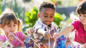 Three kids painting bird houses outside on a sunny day