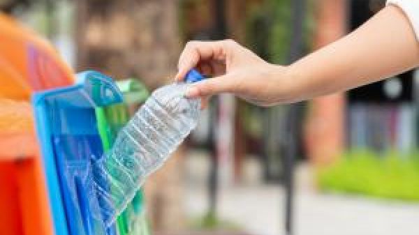 A hand dropping a plastic bottle into a recycling bin.