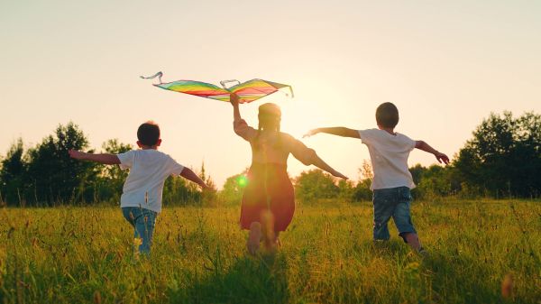 Three children running outside, one has a kite.