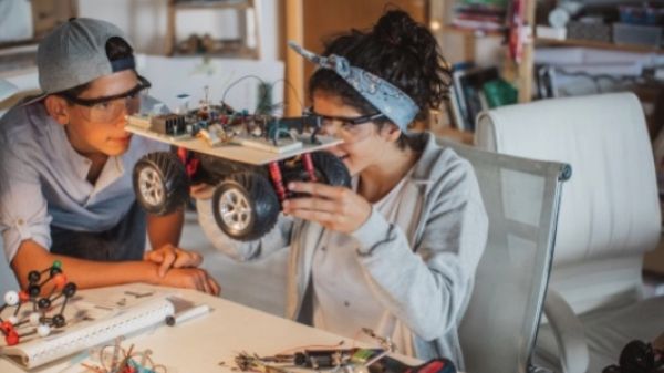 Two people building an electric vehicle model using recycled materials