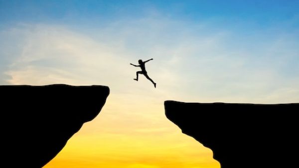 Person leaping over a chasm at sunset