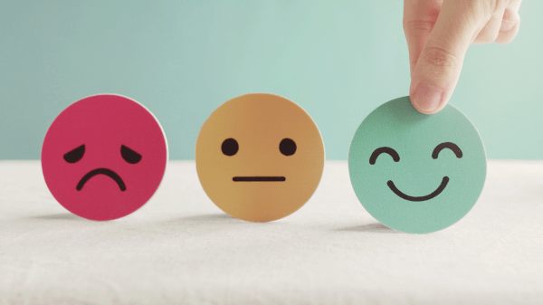 Emotions Three circles with simple faces on them sit in front of light green and white background: a red circle with a frowning face, a yellow circle with a neutral face, and a green circle with a smiling face; the green circle is being picked up by a hand