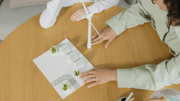 Two people sit at a table with a paper town and miniature wind turbine