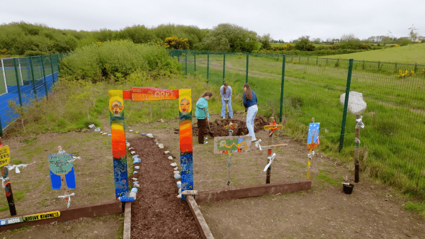 Three kids dig into the soil of a garden