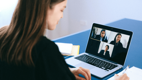 Video Call A person sits to the left with an open laptop on a blue desk in front of them; the laptop is open to a video call with three people