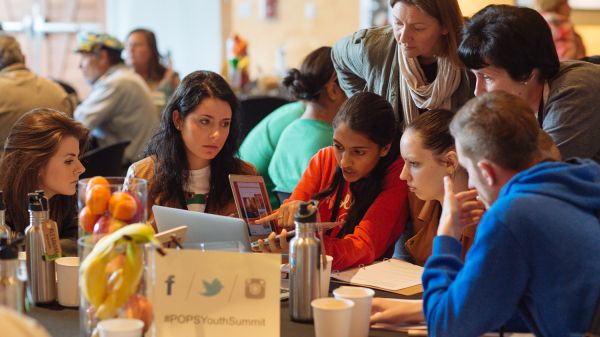 Students with a teacher talking about a lesson plan on a laptop