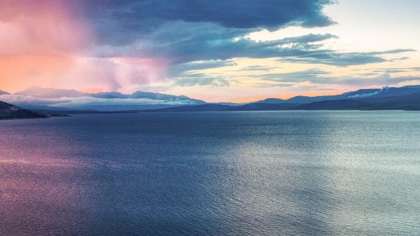 Overlooking large body of dark blue water with heavy blue, purple, and pink clouds in the distance.