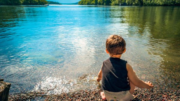 A toddler sits by the edge of a lake