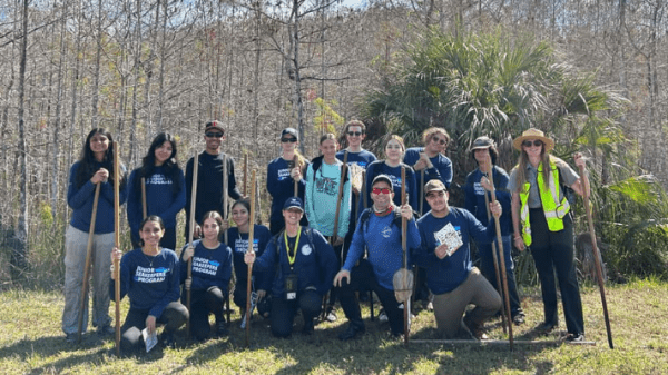 A group of Junior SeaKeepers posing in a grassy field with leafless trees behind them