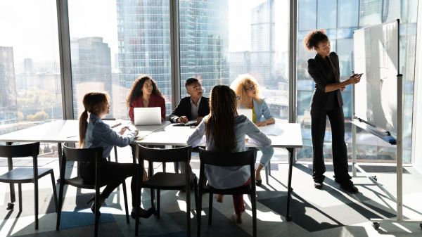 Professional Development A group of 5 people sit around a rectangular table, all facing another person standing in front of a presentation board