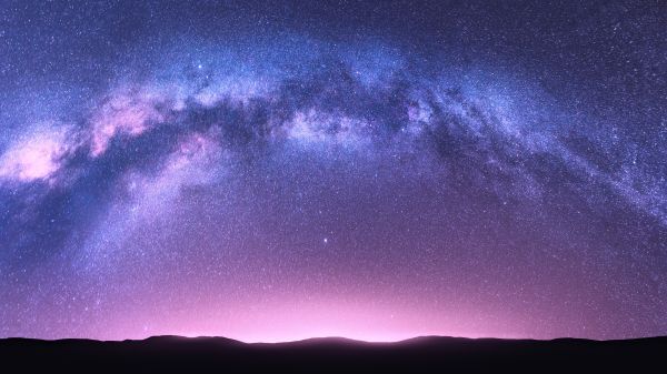 Night landscape with bright arched milky way, purple sky with stars, pink light and hills.