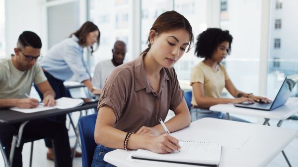Environmental Education in Higher Education A classroom has four students sitting at a desk, with an instructor leaning over the desk of the back student