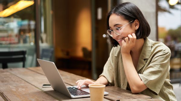 A woman with short hair and wearing glasses, smiles while looking at her laptop