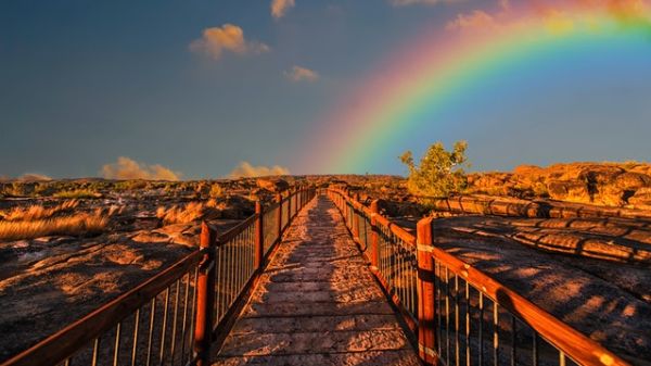 Photo of stone bridge in a rocky landscape with a rainbow arching from the center of the photo to the right