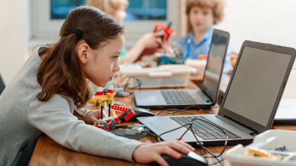 Girl using a laptop while assembling a robot from plastic bricks.