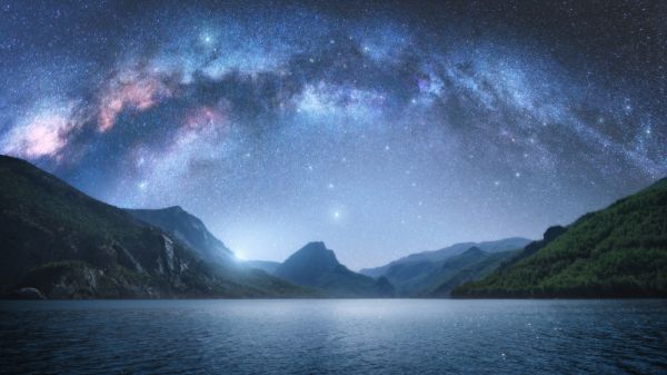 Arched Milky Way over the beautiful mountains and blue sea at night in summer. Colorful landscape with bright starry sky with Milky Way