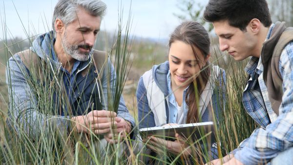 teacher with high school students looking at laptop in field