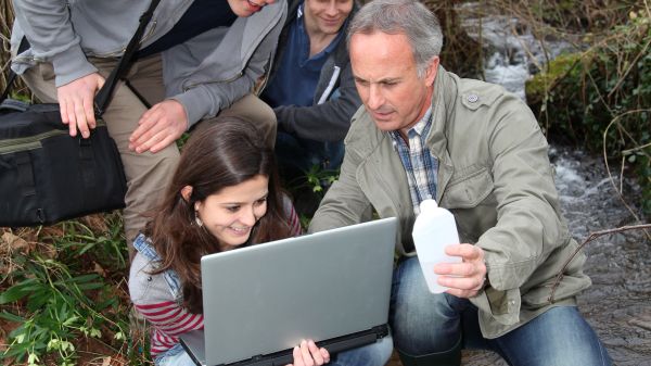 teacher and students looking at laptop at rivers edge