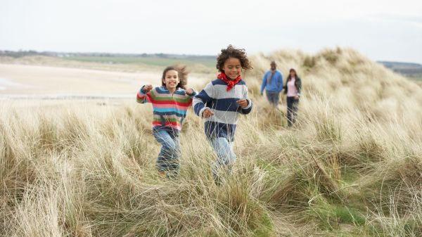 Two young kids and two adults walk along path in high grass.