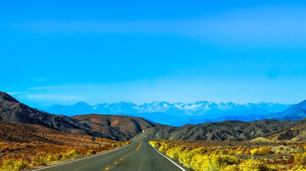 A highway road leading away from the viewer to hills and a mountain range in the distance