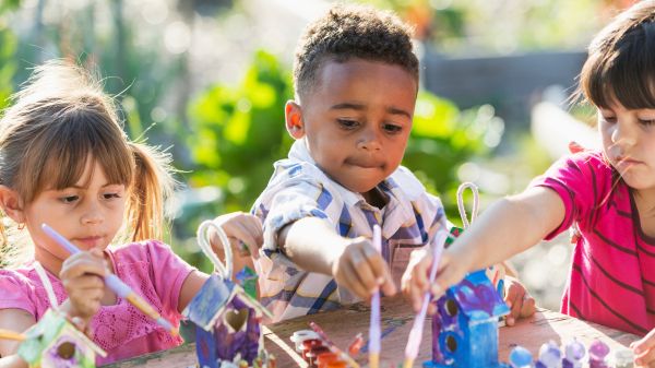 Three kids painting bird houses outside on a sunny day