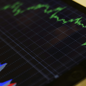 A tablet sits on a table; at the bottom of the screen is a graph with three alternating colors: blue, red, and gray; at the top is a varying bright green line