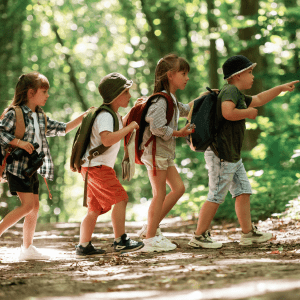 Four children wearing backpack hike a path in a green forest