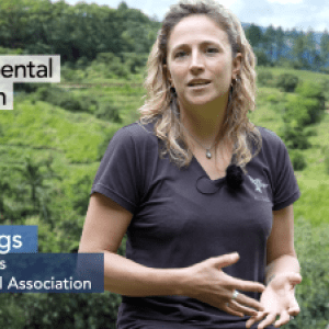 Lilly Briggs speaking, tropical forest in the background. "Environmental Education" "Lilly Briggs, Finca Cántaros Environmental Association"