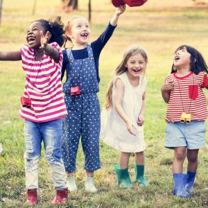 Preschool aged children outside lined up horizontally, jumping and laughing 