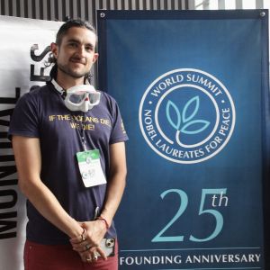 Billion Acts of Peace Fellowship Mentor at Monterrey, Mexico 2024; two people stand on either side of a "25th Founding Anniversary, World Summit Nobel Laureates for Peace" banner