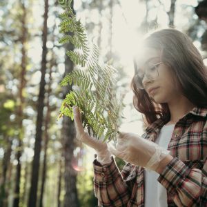 Child holds a magnifying glass to a fern