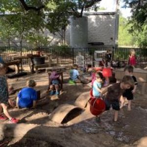 Young children playing in an outdoor sand and water area with a variety of loose parts
