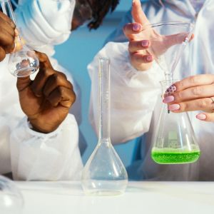 Zoomed in picture of two people in white lab coats holding test tubes and beakers over a white table
