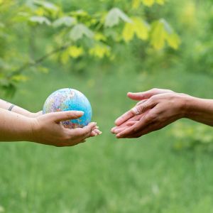 Two hands to the left pass a small globe to two hands to the right, behind them is a green plant-filled background