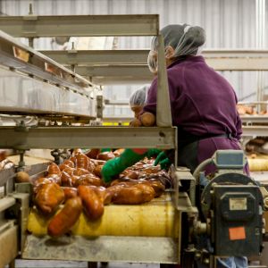 A person wearing a hair net and gloves cleans sweet potatoes on metal shelving