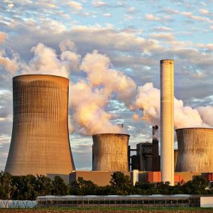 A factory with a number of smokestacks in front of a blue cloudy sky