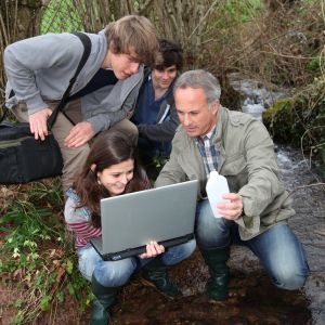 teacher and students looking at laptop at rivers edge