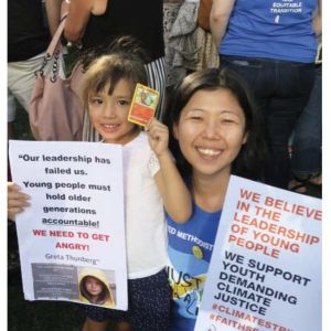 An East American American woman and her daughter at a climate change rally holding signs about faith communities and young people demanding climate action